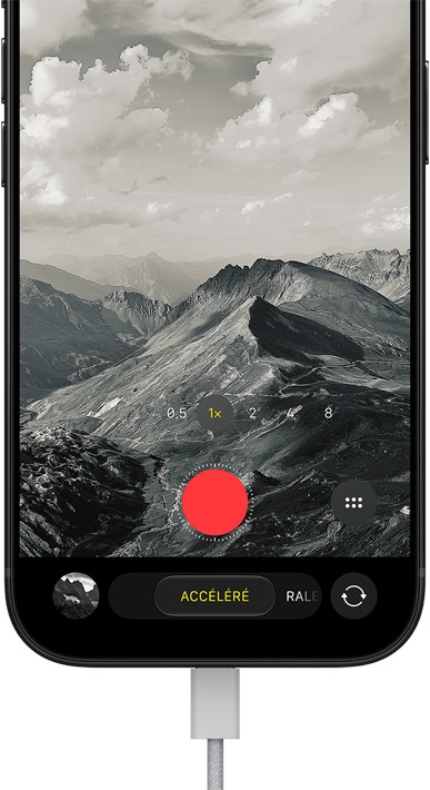 Un iPhone 18 Pro, face avant, affichant un paysage montagneux, avec le menu superposé du mode caméra en mode accéléré, câble d’alimentation branché au port de recharge