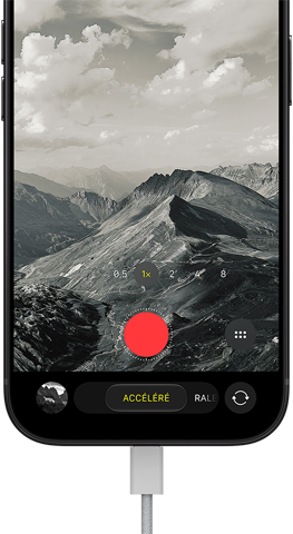 Un iPhone 18 Pro, face avant, affichant un paysage montagneux, avec le menu superposé du mode caméra en mode accéléré, câble d’alimentation branché au port de recharge