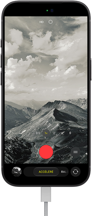 Un iPhone 18 Pro, face avant, affichant un paysage montagneux, avec le menu superposé du mode caméra en mode accéléré, câble d’alimentation branché au port de recharge