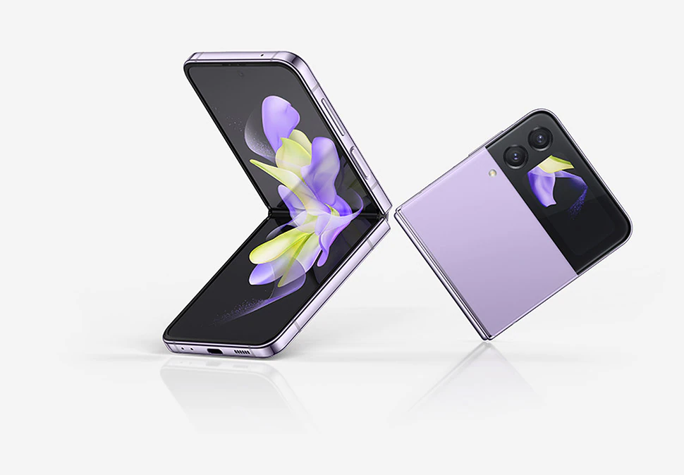 Two Bora Purple GalaxyZFlip4 devices are next to each other. One is open at a 90 degree angle and its Main Screen displays a purple and yellow ribbon-like wallpaper. The other is folded and its Cover Screen features the same wallpaper as the Main Screen on the other device.