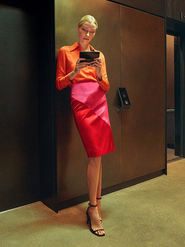 A woman stands by
						an elevator, holding an unfolded Galaxy Z Fold4 and looking at its Main Screen intently.