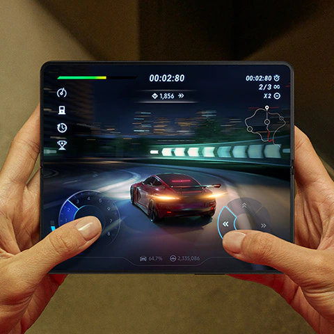 Hands holding an
						unfolded Galaxy Z Fold4. The Main Screen displays a scene from a racing game. A sports car speeds down a highway
						with a dashboard overlay on the screen. The content is smooth.
