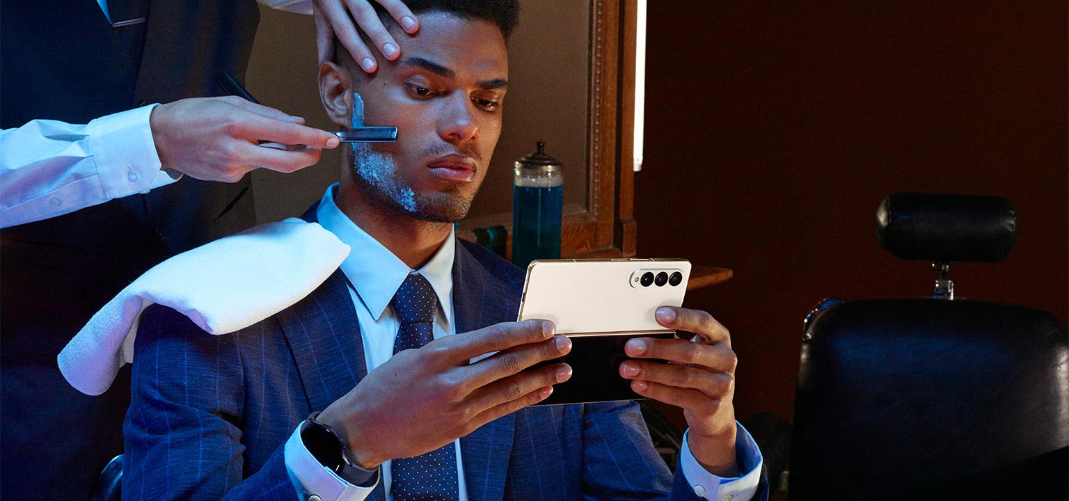 A man holds
					Galaxy Z Fold4, unfolded while sitting in a barber's chair.
