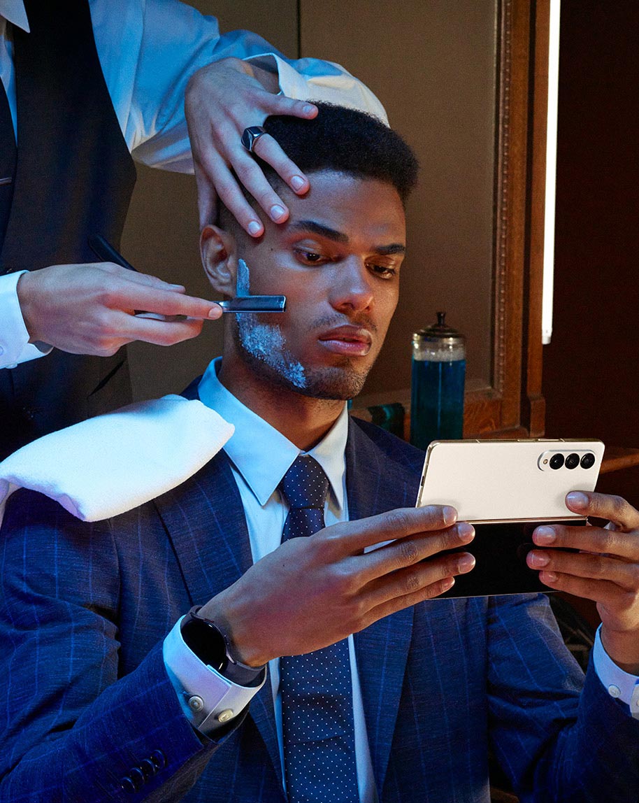 A man holds
					Galaxy Z Fold4, unfolded while sitting in a barber's chair.