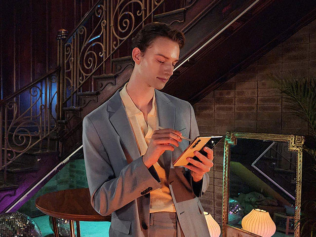 A man
				stands next to a stairwell in a dimly lit lounge, looking at the Main Screen of a Galaxy Z Fold4 in his hand.
				Nightography makes the colours bright and details of the subject and background clear even in a dark setting.