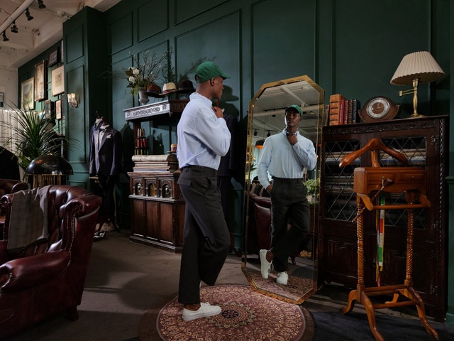 A man stands
			in a tailor shop and looks at his reflection in a mirror.