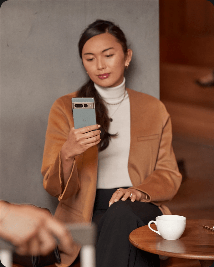 A person drinking coffee looks at their Pixel 7 Pro