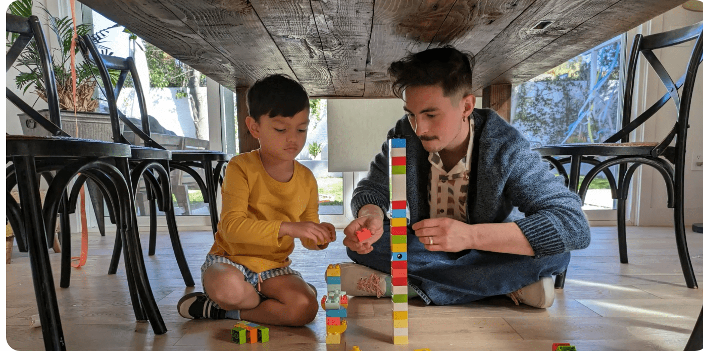 A person and a child play with toys under a table, showing how the main camera captures stunning details even in low light.